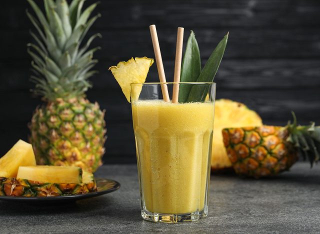 Tasty pineapple smoothie and sliced fruit on grey table, closeup