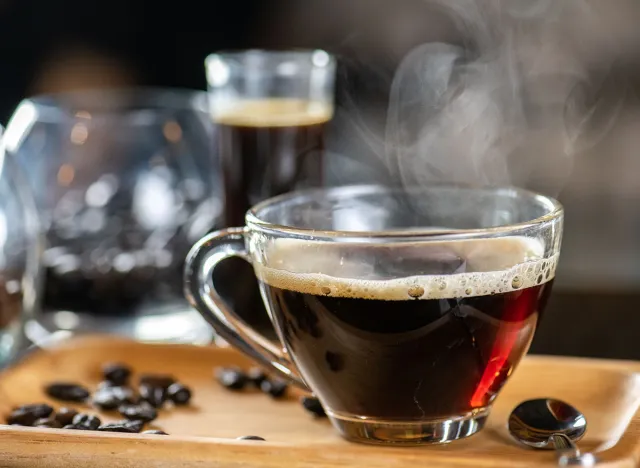 black drip coffee in glass cup, Barista making drip coffee by pouring spills hot water on coffee bean. Barista serve holding cup of hot black coffee or americano for serve on wooden table cafe shop