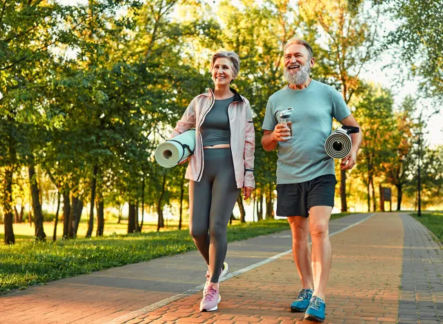 Beautiful sporty healthy active cheerful smiling middle-aged couple going to workout outdoors in park holding mats for yoga, pilates, gym. Sports healthy lifestyle. Friends on a morning walk.