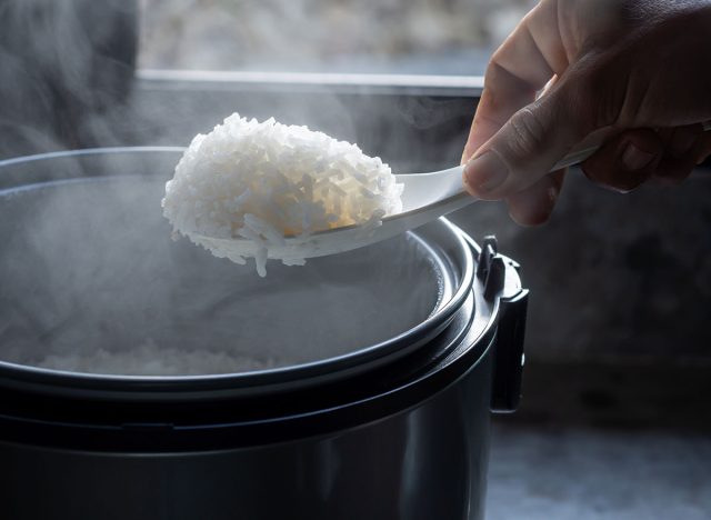 Jasmine rice cooking in electric rice cooker with steam on dark background. Soft Focus,