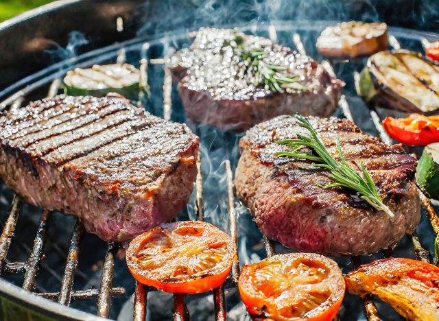 delicious grilled steak meat with vegetables on barbecue grill with smoke and flames. popular outdoor summer activity for friends and family