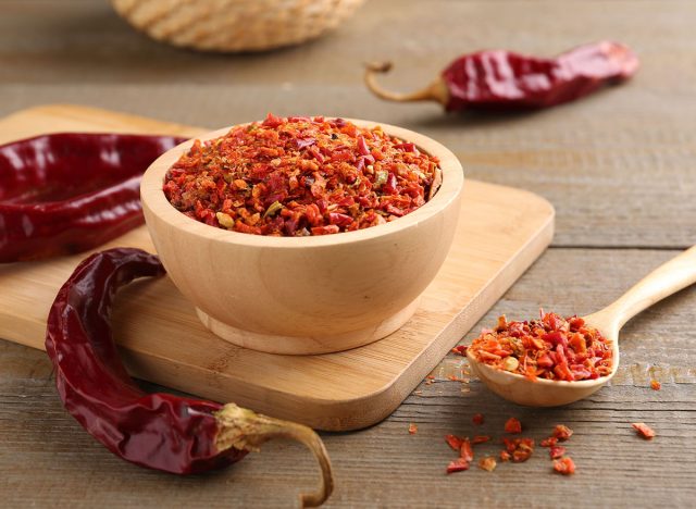 Aromatic spice. Red chili pepper flakes in bowl, spoon and pods on wooden table