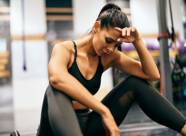 Fit girl has a headache, feels tired during a workout at the gym, holding her head.