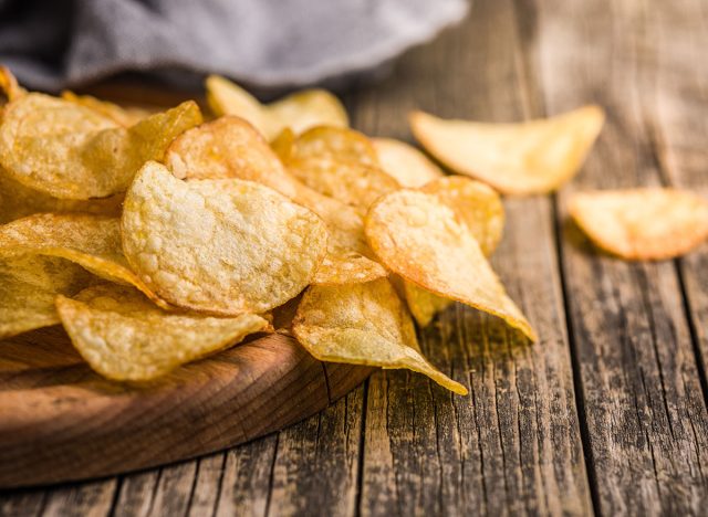 Crispy Potato Chips on cutting board on a wooden table.