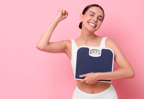 Diet and weight loss concept. Happy young woman with floor scale on pink background. Space for text