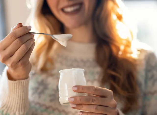 Close up of happy beautiful woman eating yogurt while standing in living room at home