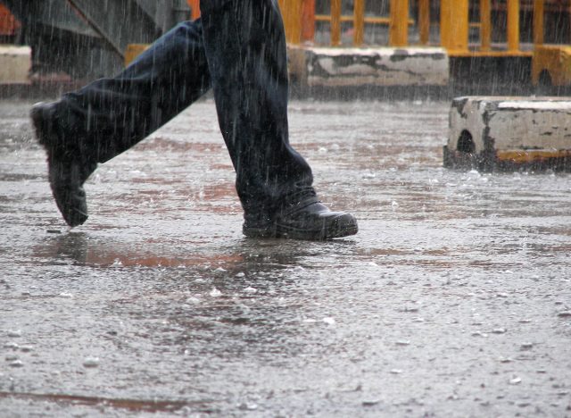 Man wearing jeans and working shoes walking under the heavy rain