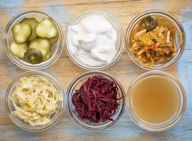 a set of fermented food great for gut health - top view of glass bowls against grunge wood: cucumber pickles, coconut milk yogurt, kimchi, sauerkraut, red beets, apple cider vinegar