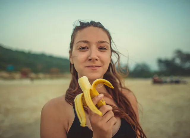 Girl eating banana on the beach against the backdrop of the hill