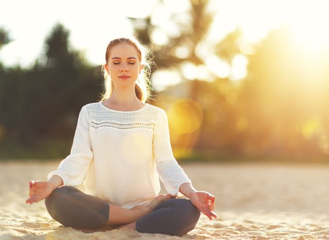 woman practices yoga and meditates in the lotus position on the beach