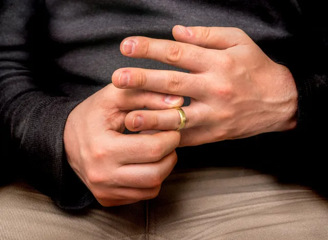 Disappointed man is taking off his wedding ring isolated on black - divorce concept