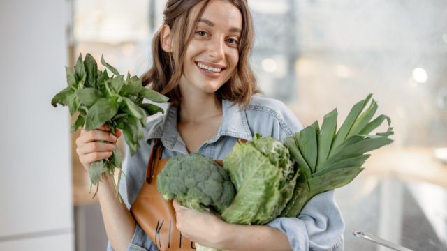 Portrait of pretty smiling woman with fresh broccoli, roman salad, basil on the kitchen with steam on background