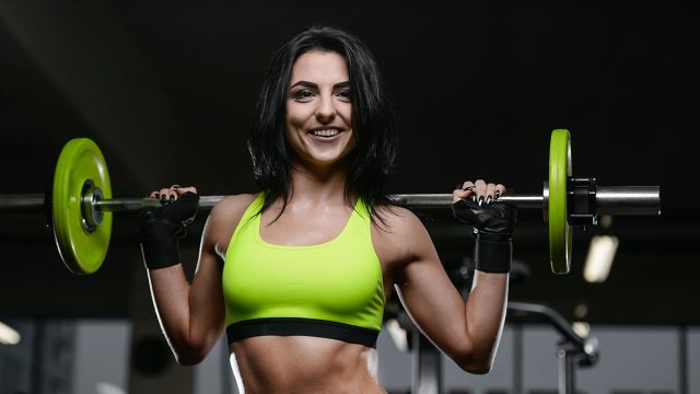 Beautiful brunette sexy athletic muscular young brunette Caucasian fitness girl working out training in the gym gaining weight pumping up abs muscles and poses bodybuilding health care concept