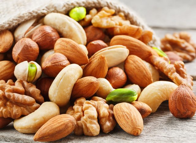 Mix of different nuts in a wooden cup against the background of fabric from burlap. Nuts as structure and background, macro. Top view.