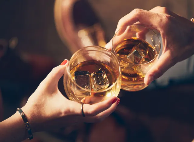 A couple makes a toast with two glasses of whiskey