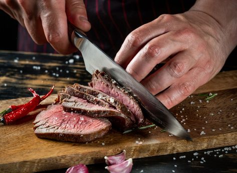 Cooking juicy beef steak by chef hands on dark black background with copy space for text menu or recipe.