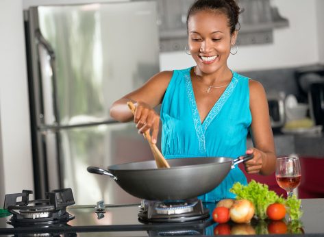 Smiling Indonesian woman stirring food in wok in kitchen