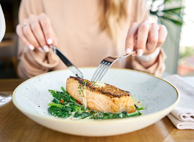 Salmon steak fillet with grainy mustard and spinach. Lunch in a restaurant, a woman eats delicious and healthy food. Restaurant menu, a series of photos of different dishes