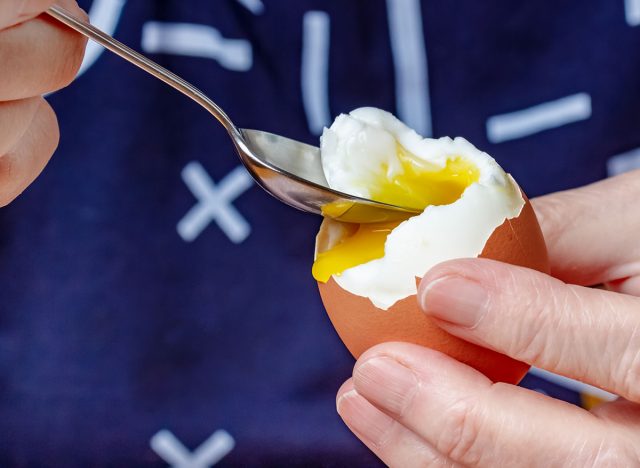 Teaspoon in the boiled chicken egg body with liquid yolk in the woman hands close-up