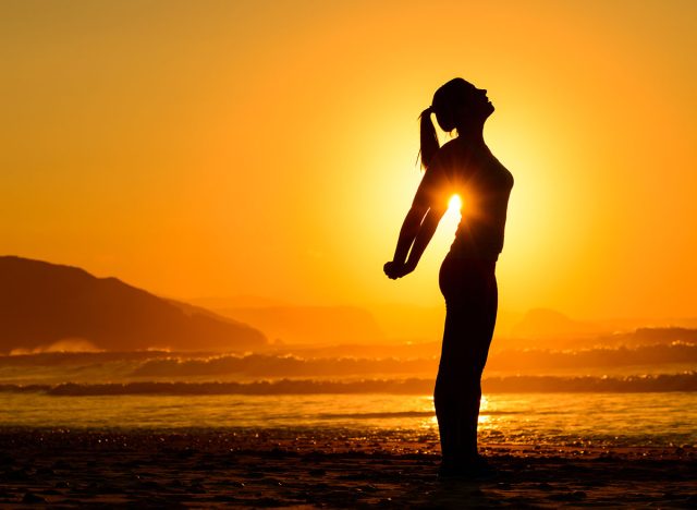 Fit woman doing yoga relaxing and breathing exercises on beach at sunset. Freedom, relax and harmony in nature. Female stretching arms alone.