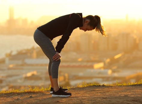 Profile of an exhausted runner resting after running in city outskirts at sunset