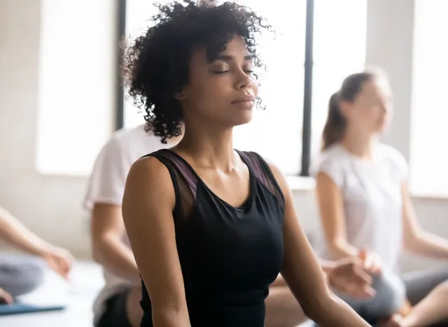 Yoga class concept, close up focus on mixed race African female closed eyes do meditation practice with associates during session. No stress, reducing fatigue after work out sport activity, wellness