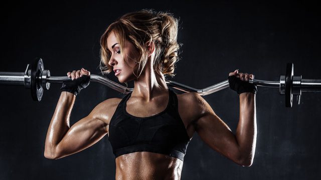 Brutal athletic woman pumping up muscles with barbell