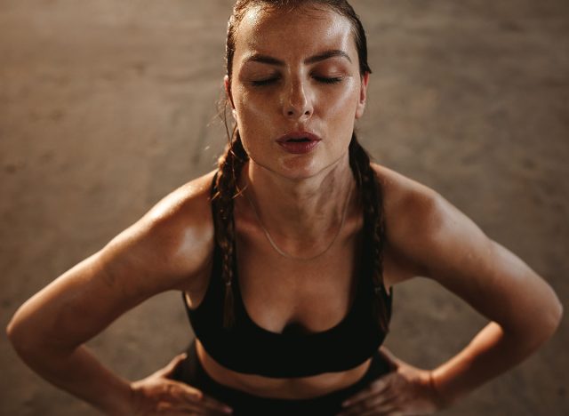 Fit woman with her hands on her hips taking deep breathe. Female athlete taking break after intense workout.