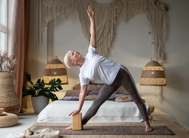 Senior woman practicing yoga, stretching in Utthita Trikonasana exercise, extended triangle pose, working out at home.