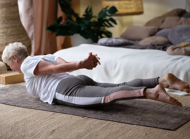 Senior woman practicing yoga at home indoor, doing Salabhasana or Locust pose. Wellness and healthy lifestyle