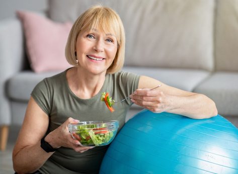 Exercise and healthy diet concept. Senior woman with fitball eating fresh vegetable salad at home. Mature Caucasian lady having veggies after sports training, keeping weight loss diet