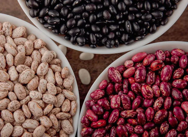 The photo shows red, white, black beans. The texture of the seeds is made in high resolution HD. The background of the beans is brown. The beans are in 4 bowls .