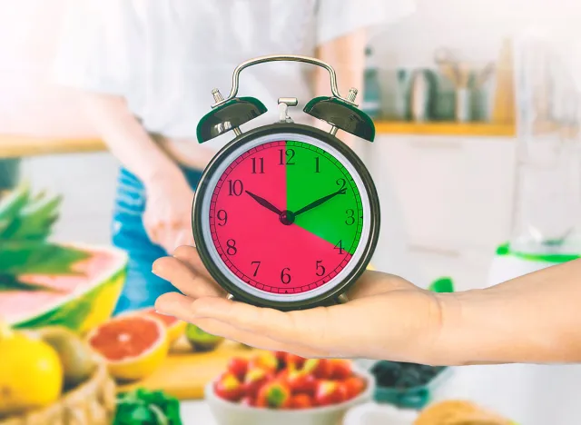 Hand holding a clock in a kitchen. Intermittent fasting concept. Empty copy space for Editor's text.