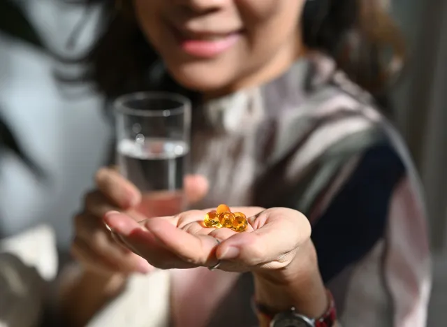 Selective focus of wrinkled hands of a senior woman holding fish oil or omega-3 supplement capsule.