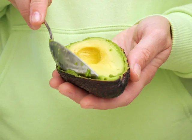 Woman shows sliced avocado. Close-up of a woman scooping out an avocado pulp with a spoon. Vegetarian food concept. Foods with vitamin E, avocado oil and antioxidants. Conscious nutrition concept.