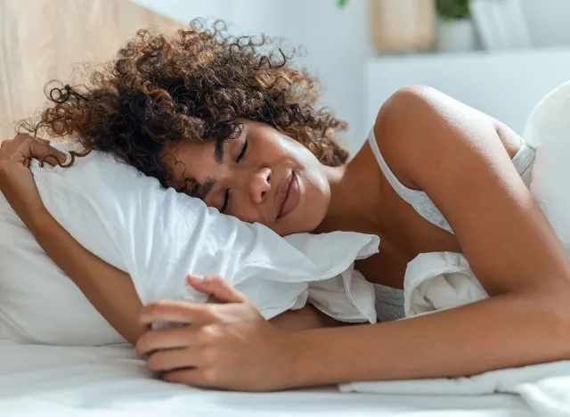 Shot of kind woman sleeping peacefully while hugging the pillow on the bed.