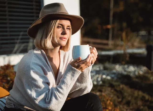 Beautiful woman in cowboy hat drinking coffee on patio in front of her house