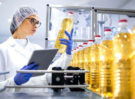 Food inspector or technologist doing quality control of bottled vegetable oil inside bottling plant.