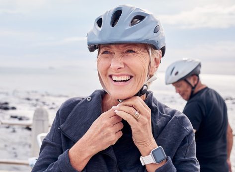 Happy senior woman, bicycle and helmet on holiday ride at beach for fitness workout with man. Smile on face, happiness and health, cycling exercise for mature couple on ocean vacation in Australia.