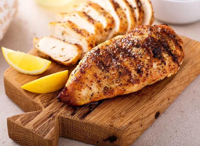 Grilled chicken breast with spice rub and lemon on a cutting board, sliced and whole