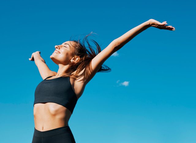 Horizontal portrait of a beautiful young fit smiling woman deep breathing in front of a clear blue sky in a sunny windy day of summer