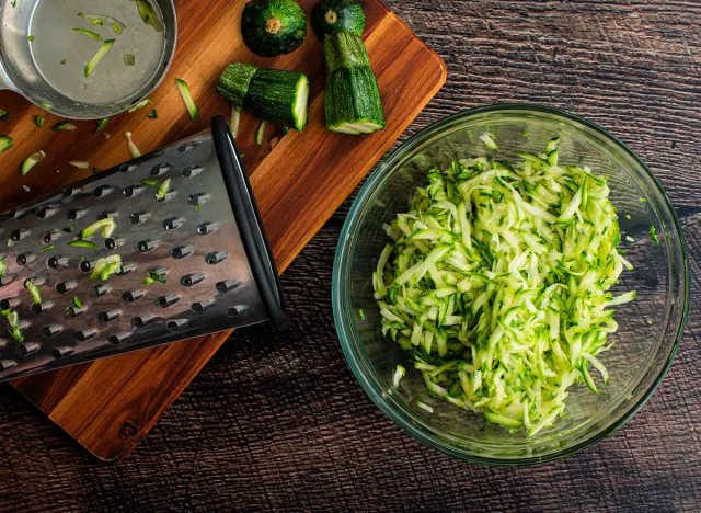 Shredded Zucchini in a Glass Mixing Bowl: Grated zucchini shown with a box grater and other tools