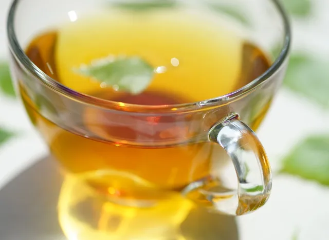 Green tea in a glass cup with a birch leaf. Leaves on a white table around a mug with a drink.