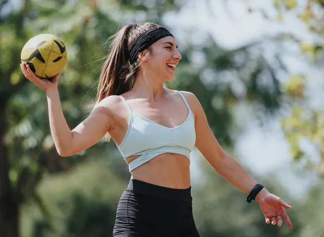 Attractive women throwing ball in sunny park, enjoying outdoor workout. Fit and sporty, they motivate each other in natural environment.