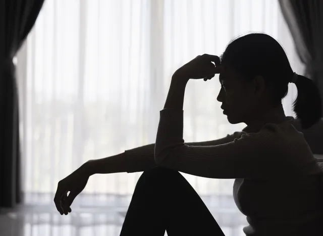 Silhouette of a person suffering from depression in the house, Depressed woman sitting alone on the Sofa feel stress, sad and worried in the dark room. person are stressed.