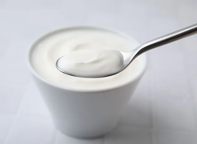 Eating delicious natural yogurt at white tiled table, closeup