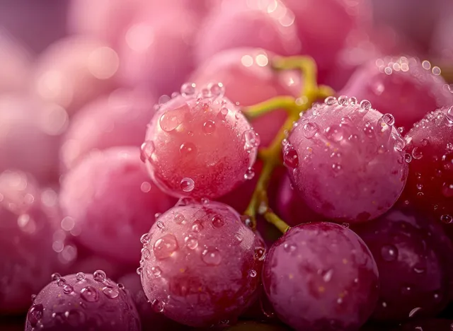 close-up of pink grapes adorned with water droplets showcases vibrant color and juicy texture. Soft lighting casts gentle shadows for a photorealistic feel.