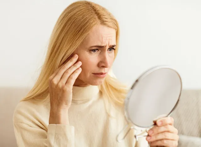 Anti-Wrinkle Skin Care. Sad Woman Looking In Mirror, Touching Her Face