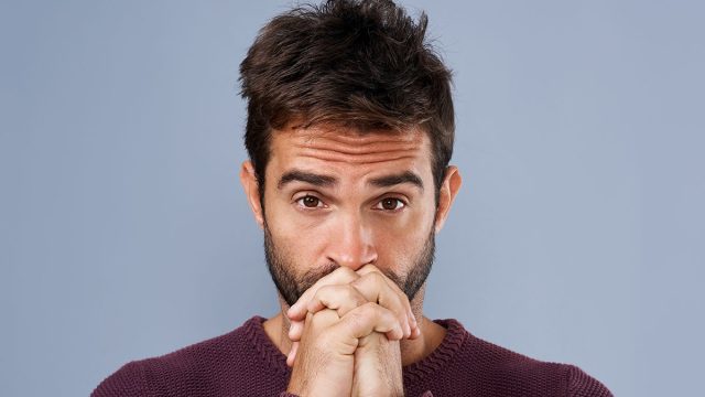 Man, portrait and anxiety prayer in studio, worry and ask God for support or help on blue background. Male person, hands together and nervous worship for assistance, religion and spiritual suspense