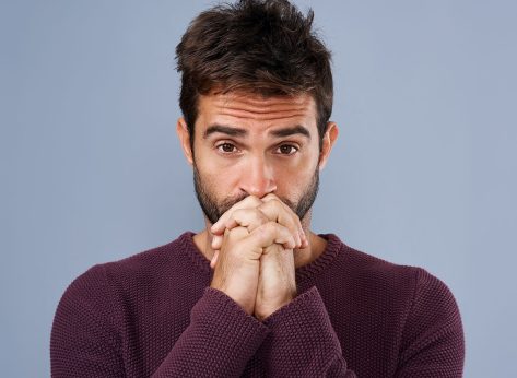 Man, portrait and anxiety prayer in studio, worry and ask God for support or help on blue background. Male person, hands together and nervous worship for assistance, religion and spiritual suspense